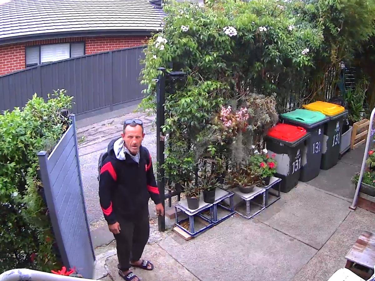 A man opens a gate and tresspasses onto property to take cans and bottles from a recycle bin.