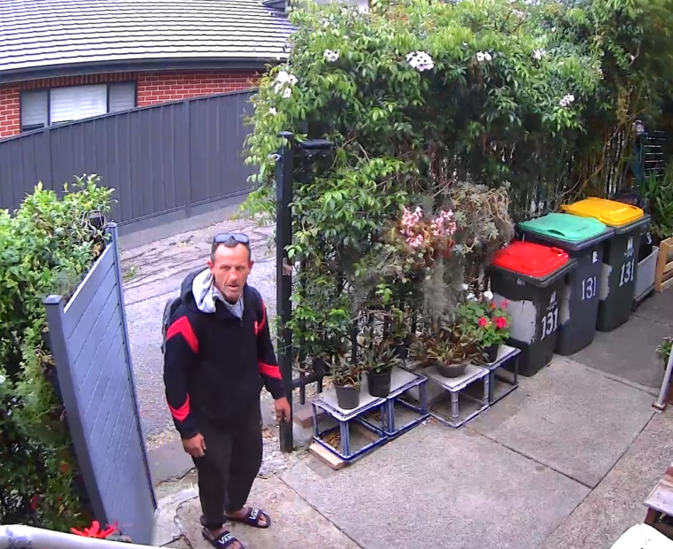 A man opens a gate and tresspasses onto property to take cans and bottles from a recycle bin.