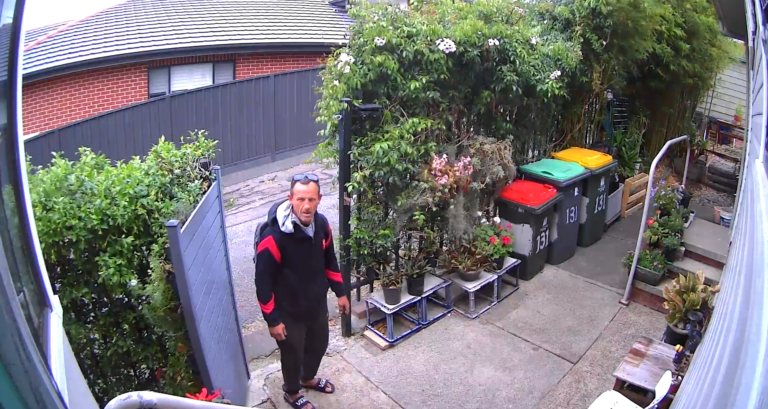 A man opens a gate and tresspasses onto property to take cans and bottles from a recycle bin.